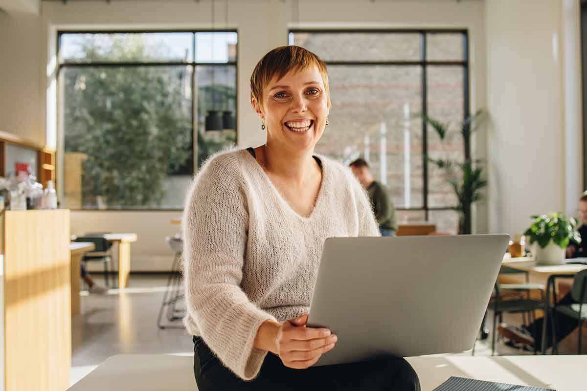 eine Frau sitzt an einem Tisch mit einem Laptop vor orangenem Hintergrund