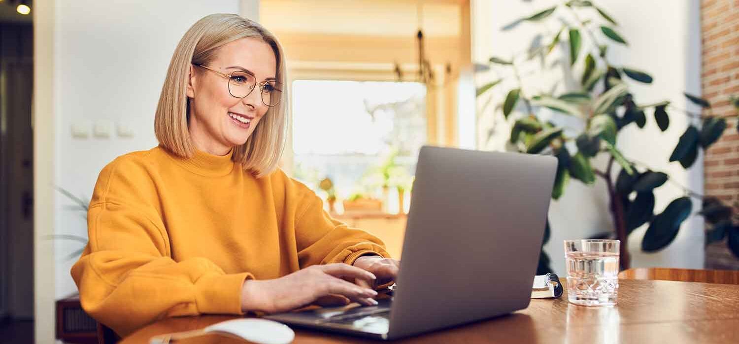 eine Frau sitzt an einem Tisch mit einem Laptop vor orangenem Hintergrund